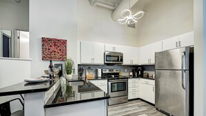 A modern kitchen with white cabinets, stainless steel appliances, a black countertop, and a unique ceiling light fixture. - Ste 713+City Views+Free Parking+Indoor Access to Skywalk (Indianapolis)