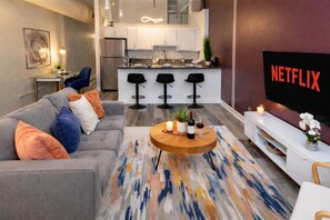Una sala moderna con un sofá gris, una mesa de centro con velas, y una cocina al fondo.