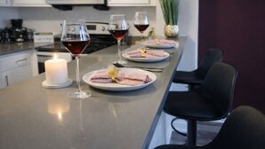 Une cuisine moderne avec un long comptoir, trois verres à vin, une bougie allumée et des serviettes pliées avec soin, disposées sur des assiettes.