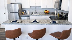 A modern kitchen with white cabinets, granite countertops, stainless steel appliances, and three brown bar stools. - Ste 404 Center of Downtown-Skywalk Access to Convention Center+Free Parking (Indianapolis)