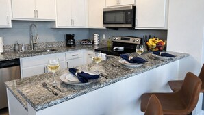 A modern kitchen with white cabinets, a granite countertop, a microwave, and a dining area set with plates, glasses, and a fruit bowl. - Ste 404 Center of Downtown-Skywalk Access to Convention Center+Free Parking (Indianapolis)