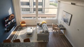 A modern living room with a sofa, chairs, a coffee table, a TV, and a large window with a city view. - Ste 404 Center of Downtown-Skywalk Access to Convention Center+Free Parking (Indianapolis)