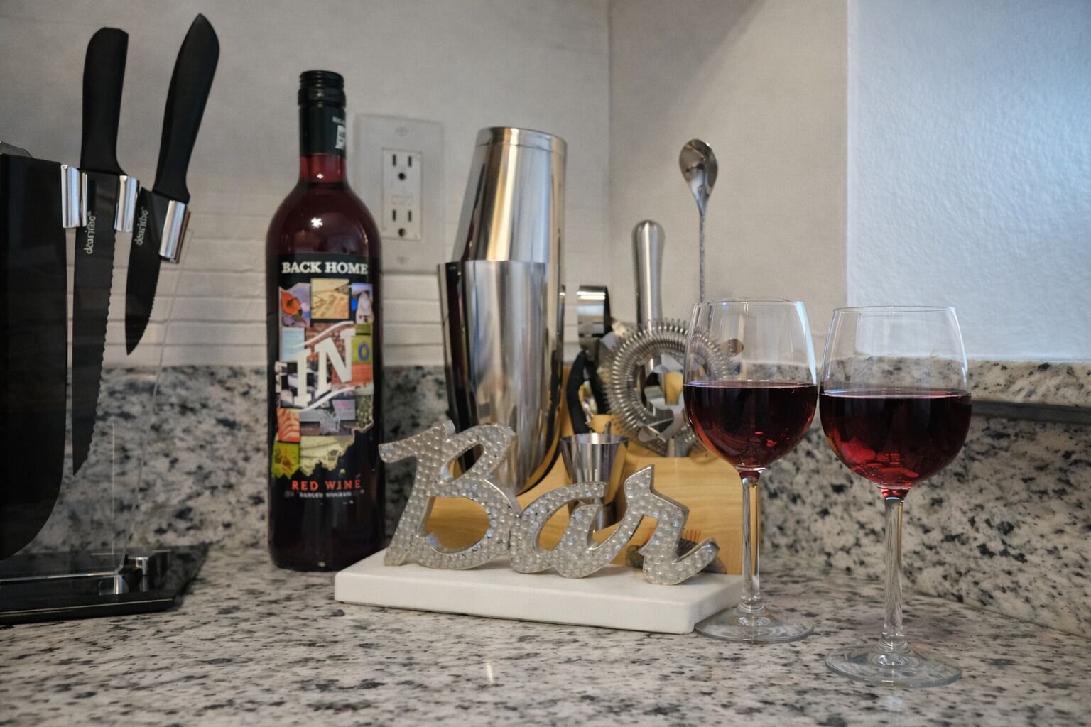Eine Küchenarbeitsplatte mit einer Flasche Rotwein, einem Cocktail-Shaker, einem Messerblock und einem dekorativen Schild.