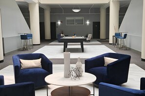 A modern lounge area with blue chairs, a pool table, and a white vase.