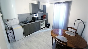 Une cuisine compacte équipée d’un four à micro-ondes, d’un évier et d’un petit réfrigérateur. On y trouve une table à manger avec deux chaises et un chemin de table décoratif.
