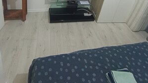 Une chambre d’hôtel avec un lit, un téléviseur posé sur un meuble, une petite table sur laquelle se trouvent divers objets, et une armoire.