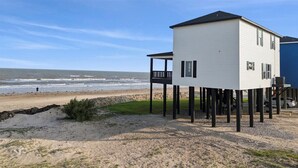 Een huis aan het strand met een balkon, verhoogd op palen, met uitzicht op de oceaan.