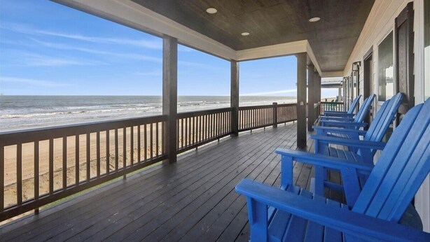 Een overdekt terras met blauwe stoelen en uitzicht op het strand.