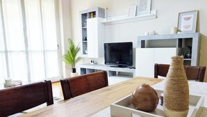 A modern living room with a wooden dining table, brown leather chairs, a TV, and a white entertainment unit with shelves.