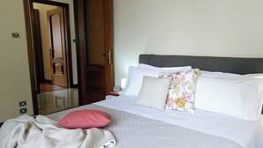 A neatly made bed with white bedding and a pink pillow, a wooden door, and a mirror on the wall.