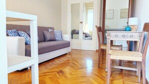 A living room with a sofa, chairs, a dining table, and a wooden floor.