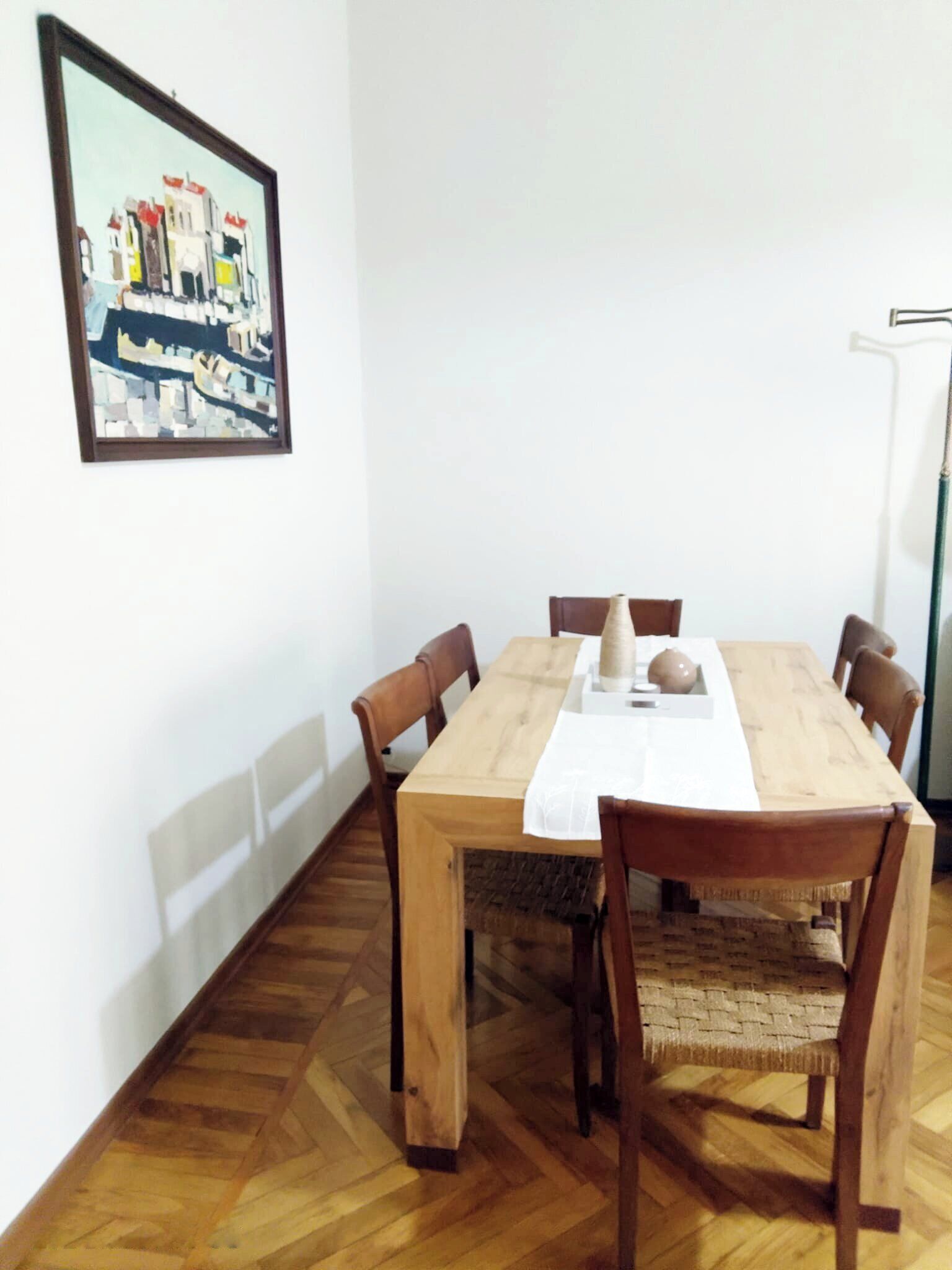 Un coin repas avec une table et des chaises en bois, une nappe blanche et un tableau encadré au mur.