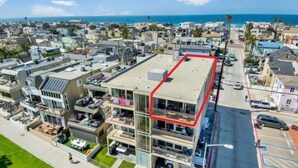 A multi-story building with a rooftop terrace, surrounded by a residential area with a view of the ocean.
