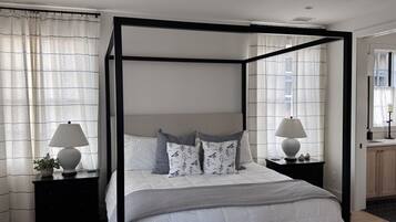 A four-poster bed with a white bedspread and gray pillows, flanked by two bedside tables with lamps and decorative items.
