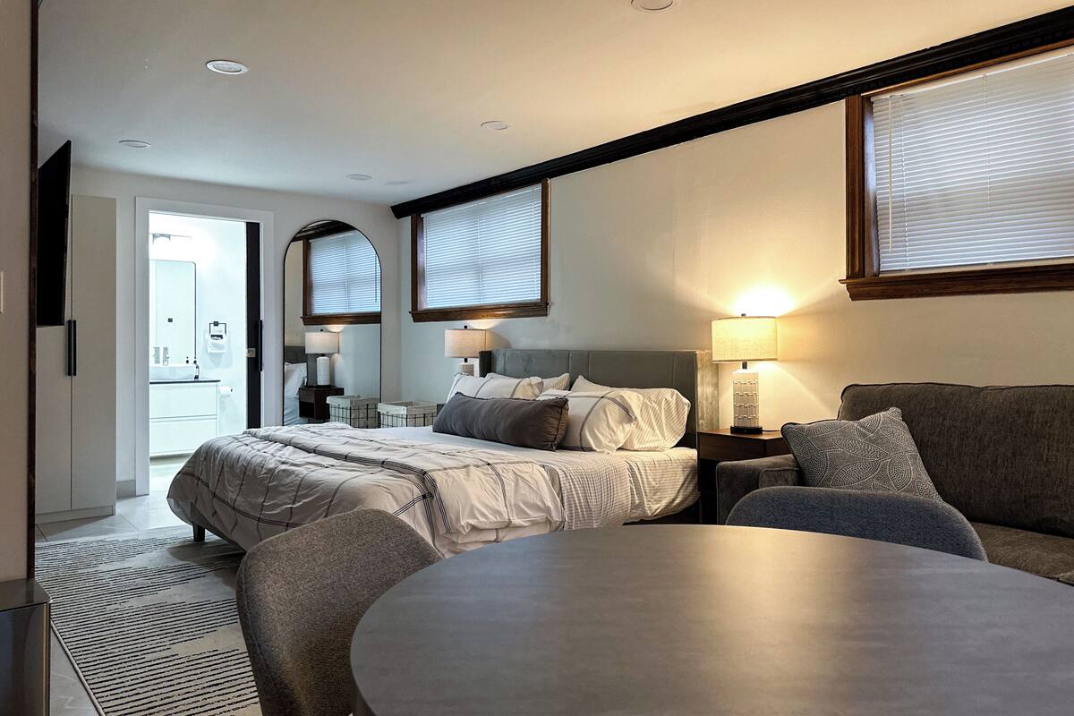 A hotel room with a bed, a sofa, a dining table, and a bathroom visible through an open door.