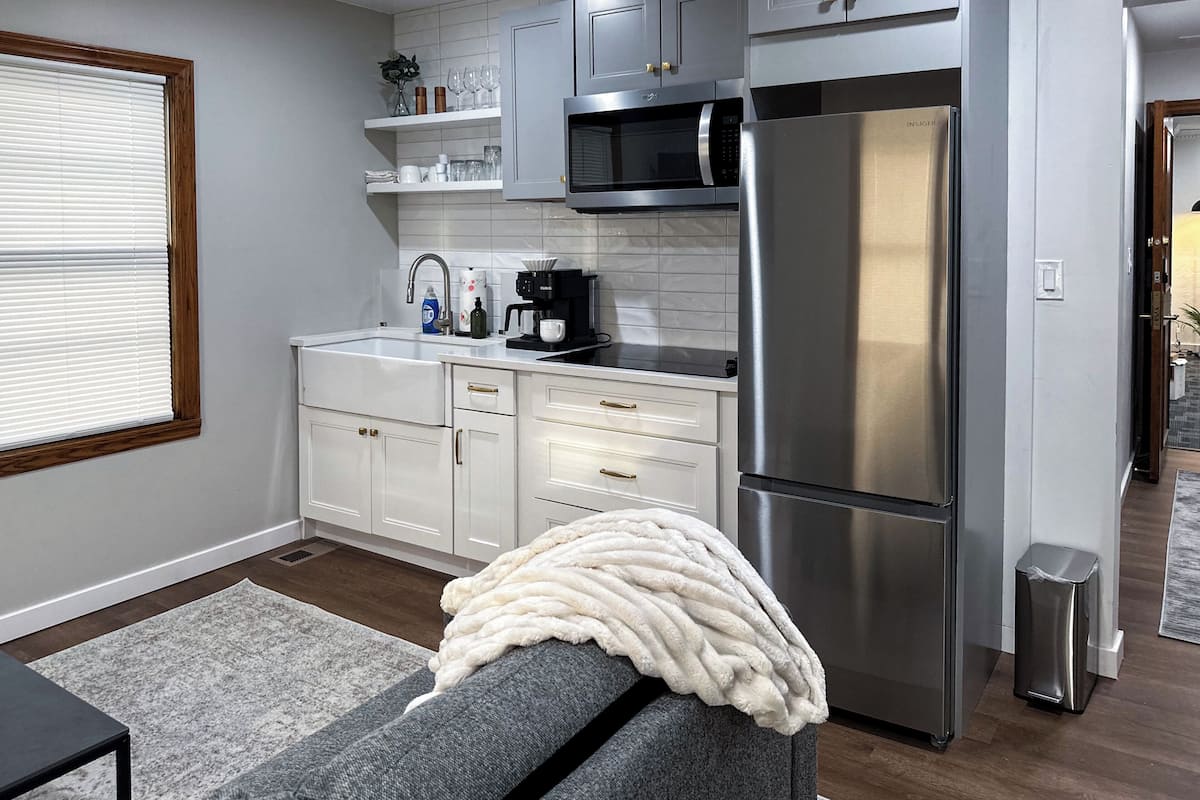 A modern kitchen with white cabinets, stainless steel appliances, and a grey sofa with a white throw blanket.