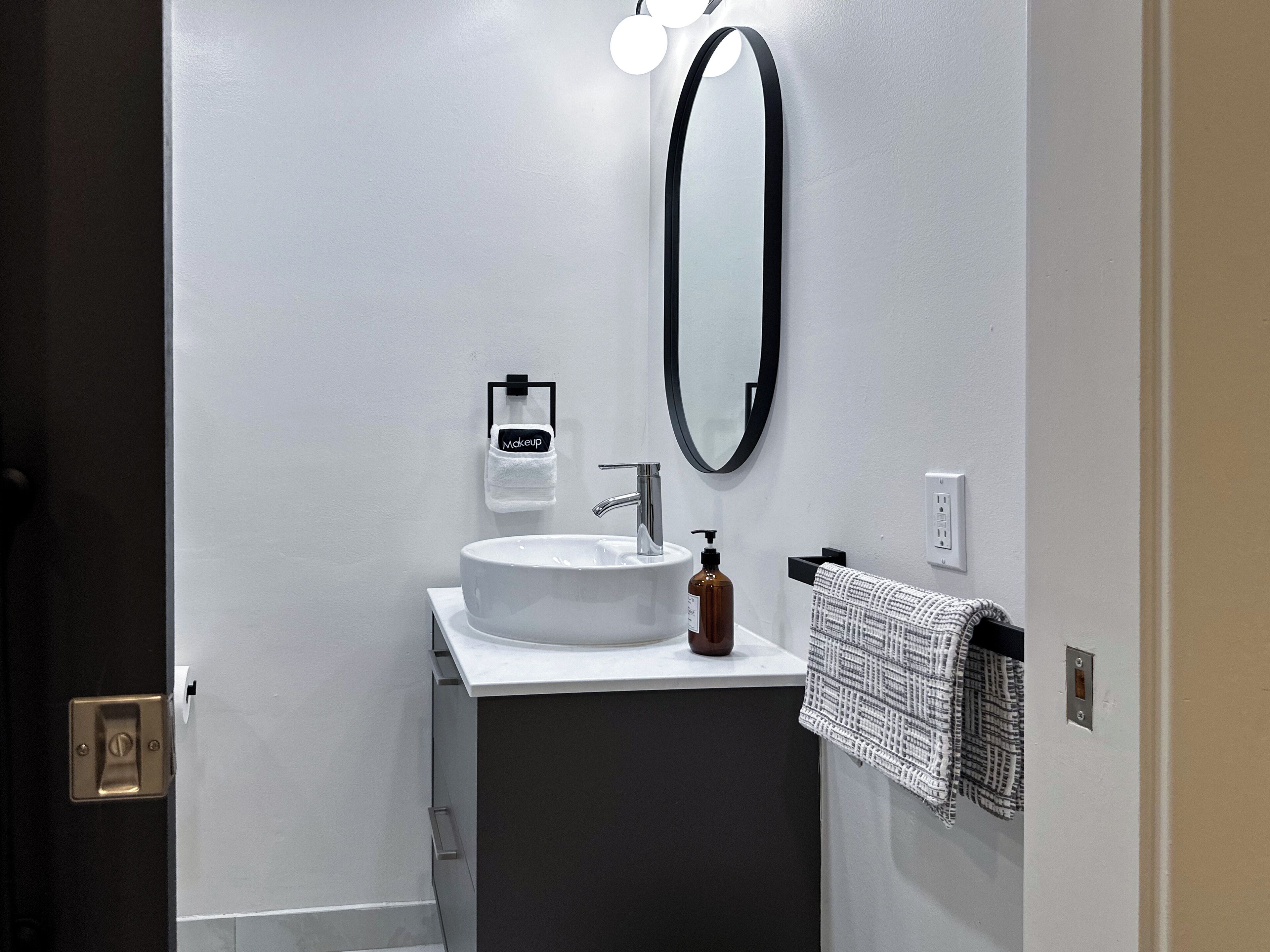 A modern bathroom with a white sink, a black-framed mirror, and a towel rack with a patterned towel.