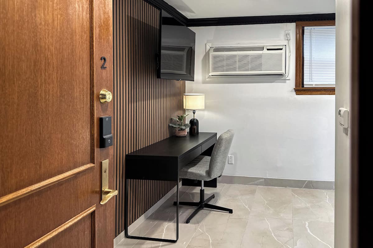 A modern office space with a wooden door, a desk with a chair, a mounted TV, and a window with blinds.