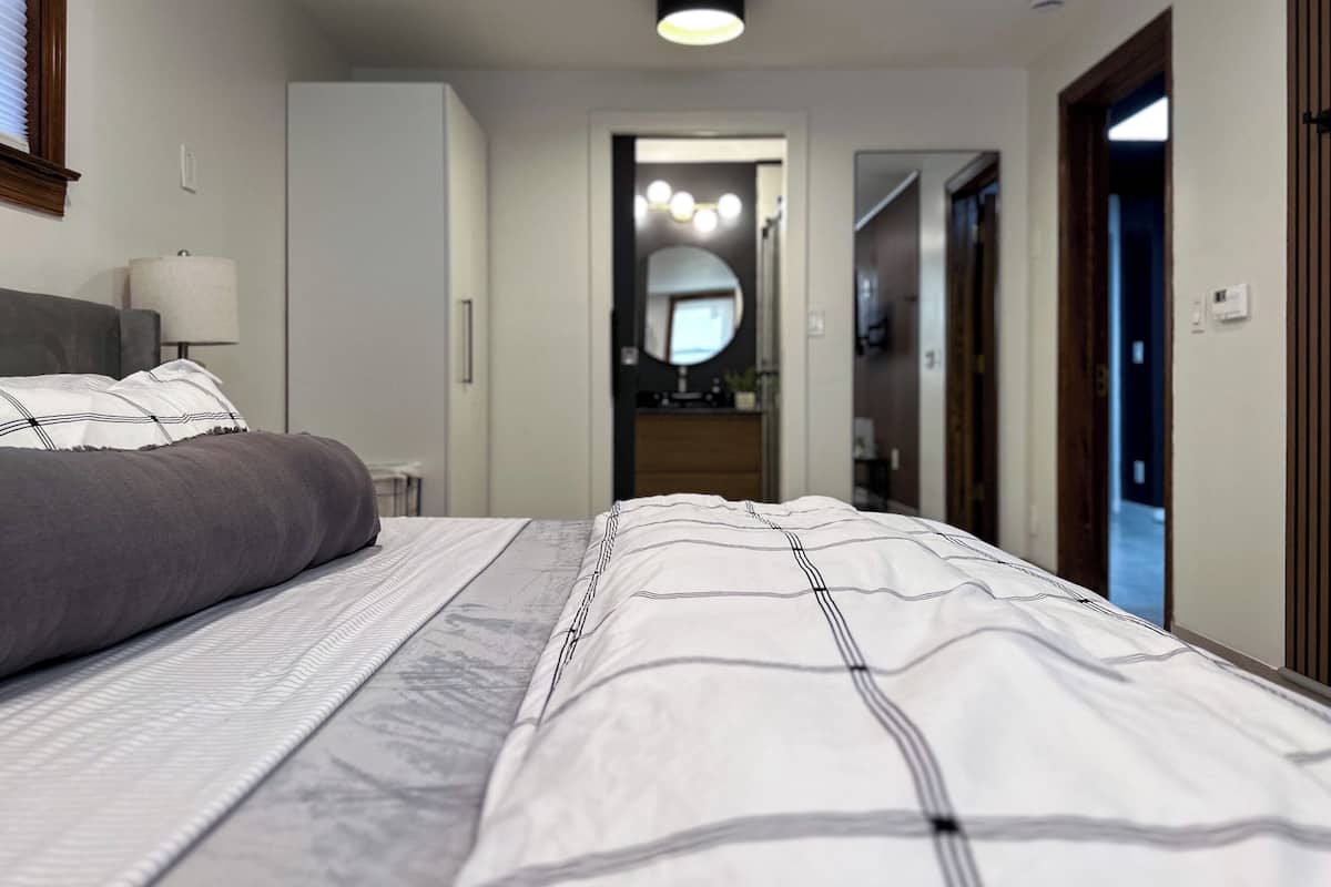 A modern bedroom with a bed, bedside table, lamp, and a view into the bathroom.