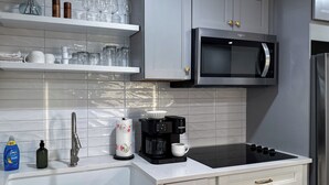 A modern kitchen with white cabinets, a stainless steel microwave, a coffee maker, and a sink.