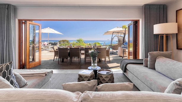 A modern hotel room with a large sliding glass door leading to an outdoor dining area with umbrellas and a view of the sea.