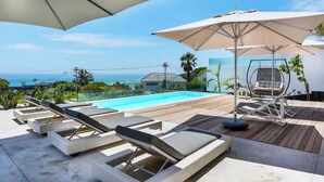 A poolside area with lounge chairs and umbrellas, overlooking a clear blue sky and ocean view.