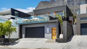 A modern two-story house with a garage, a balcony, and a mountain backdrop.