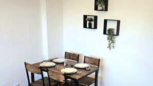 Ruokapöytä, jossa on neljä tuolia, valkoinen seinä ja pöydän yläpuolella kolme kehystettyä taulua.