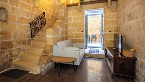A cozy living area with a stone wall, a sofa, a wooden table, a TV, and a staircase leading to an outdoor patio.