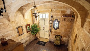 A stone-walled hallway with a wooden bench, a potted plant, and a door with a window.