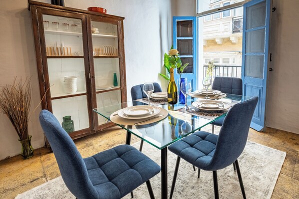 A dining area with a glass table, blue upholstered chairs, and a cabinet with glass doors.