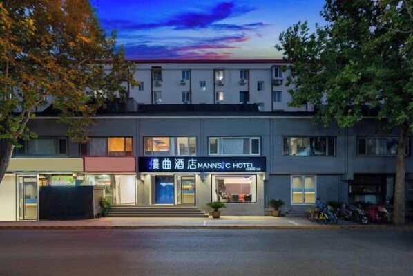 Um hotel com uma placa visível, área de estacionamento e vista para a rua.