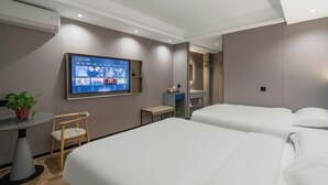 Ein modernes Hotelzimmer mit zwei Betten, einem an der Wand montierten Fernseher, einem kleinen Tisch mit Stuhl und einer Topfpflanze.