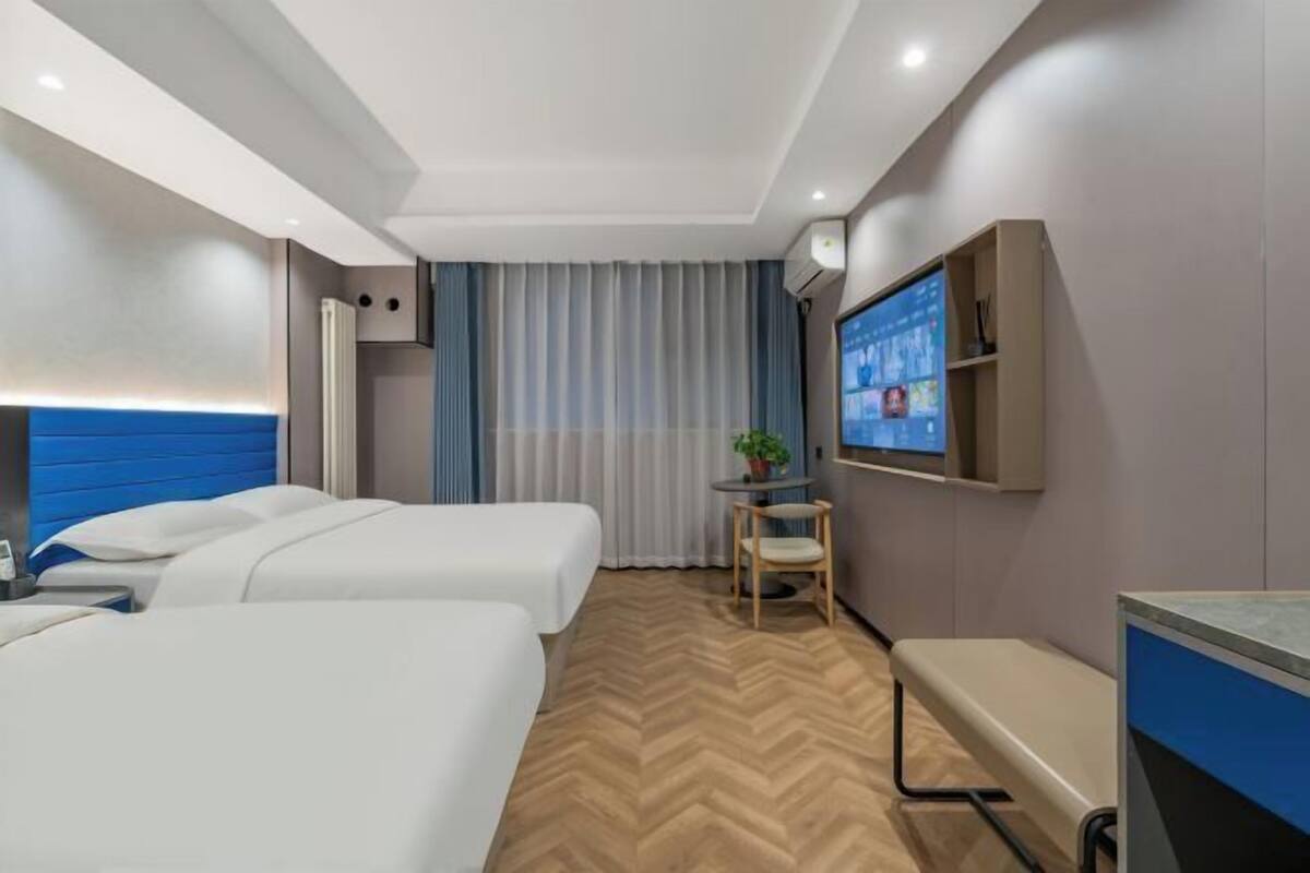 Une chambre d’hôtel avec deux lits, un bureau, une chaise, une télévision et une fenêtre avec des rideaux.