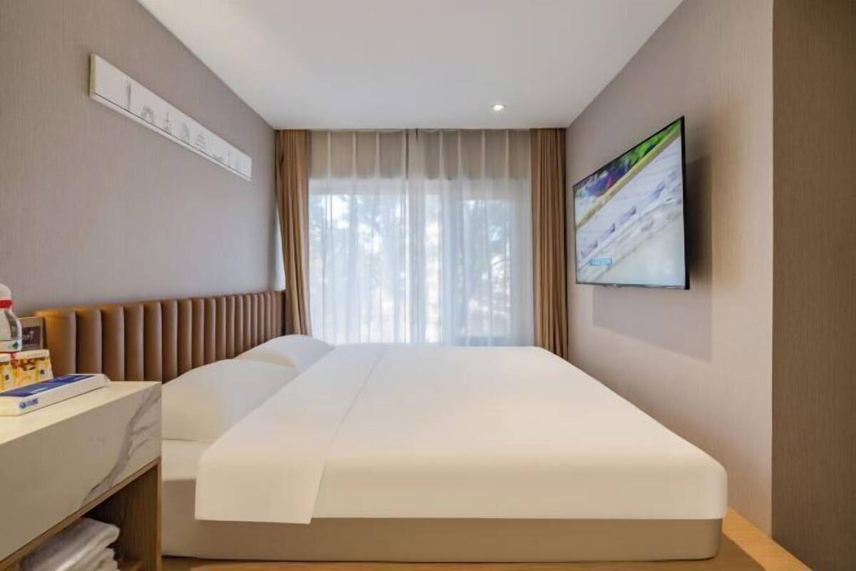Une chambre d’hôtel avec un lit, un bureau sur lequel se trouve une bouteille, un tableau encadré accroché au mur et un téléviseur fixé au mur.