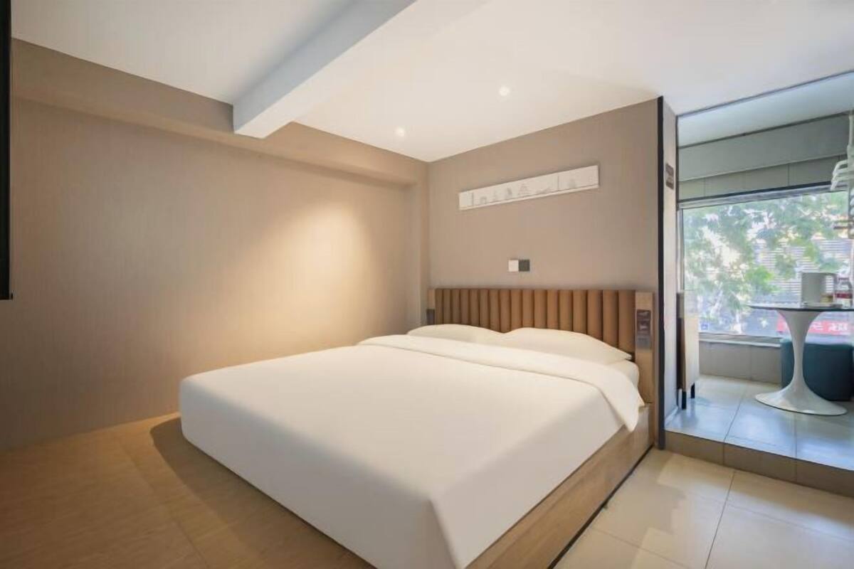 Une chambre d’hôtel moderne avec un grand lit, une tête de lit en bois, une petite table et une vue sur l’extérieur.