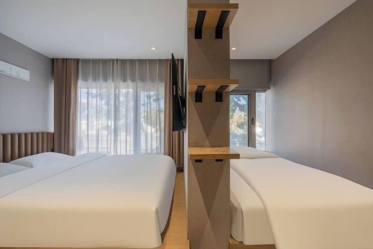 Une chambre d’hôtel avec deux lits, une cloison en bois, une télévision et de grandes fenêtres.