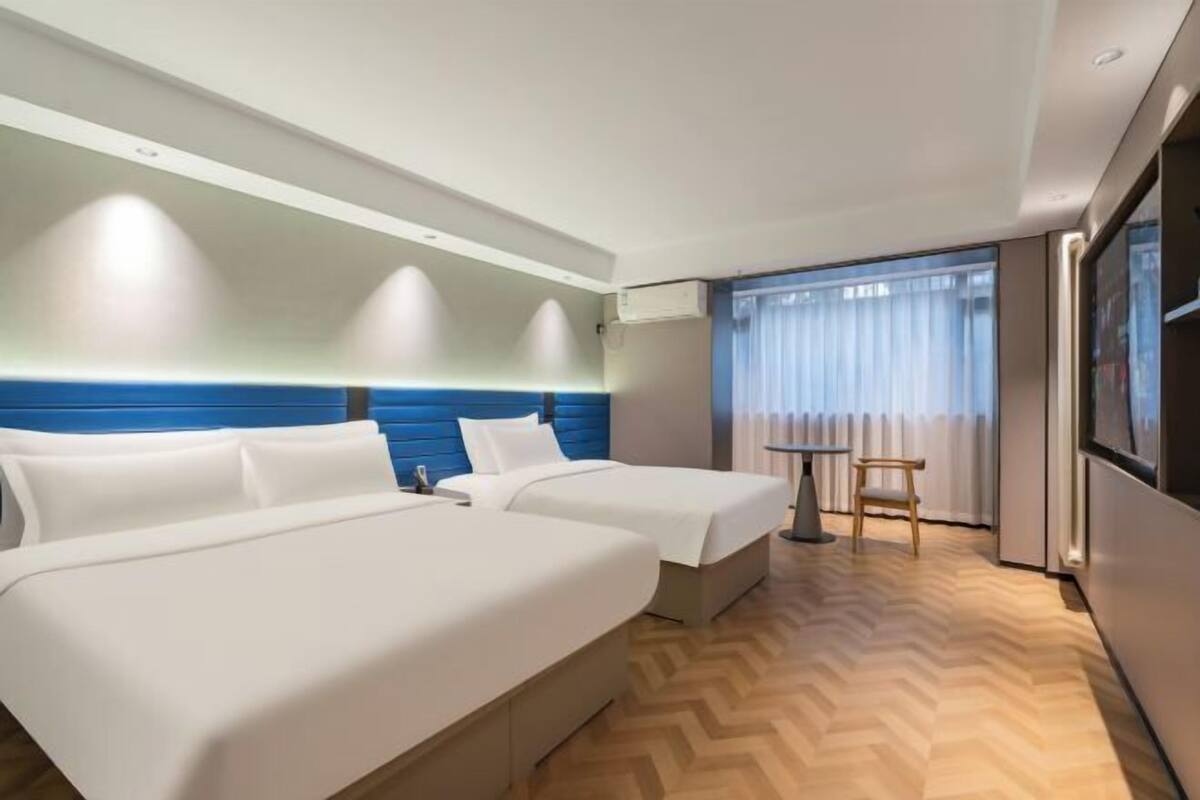 Une chambre d’hôtel avec deux lits, une petite table, un téléviseur et une fenêtre avec des rideaux.