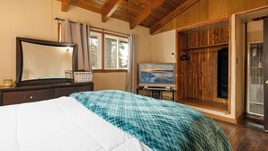 A bedroom with a bed, a TV, a wooden wardrobe, and a window with curtains.