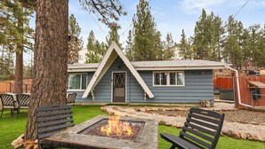 A house with a stone chimney, a fire pit, and two benches.