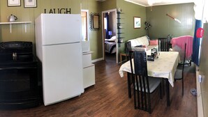 A compact kitchen with a stove, refrigerator, and a dining area with a table and chairs. - Swan #11 Graceland Cottages (Lavigne)