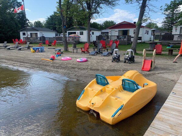 Una zona junto al lago con un muelle, botes inflables y sillas de playa.