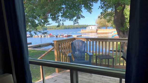 A deck with a view of a lake, a chair, and a small table. - Swan #11 Graceland Cottages (Lavigne)