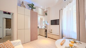 A modern living room with a sofa, a dining table set with breakfast, a kitchen in the background, and a decorative Buddha statue. - Asian Oasis with Balneo & Massage (Toulon)