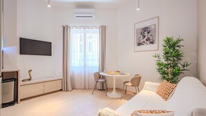 A modern living room with a sofa, a dining table with chairs, a TV mounted on the wall, and a potted plant. - Asian Oasis with Balneo & Massage (Toulon)
