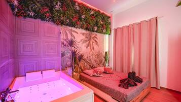 A bedroom with a bed, a large window with curtains, a wall with a tropical mural, and a wall-mounted plant arrangement.