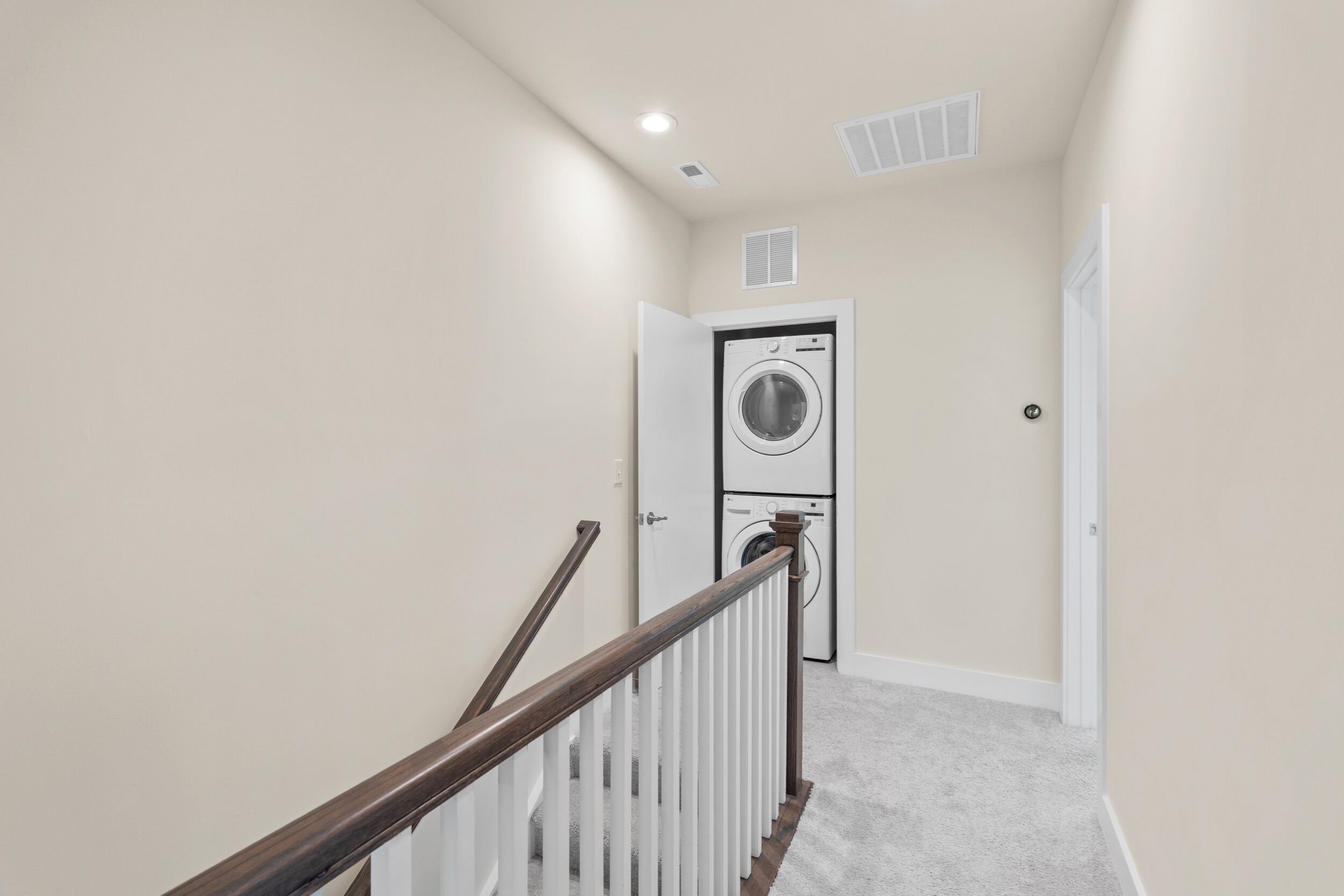 A hallway with a white door, a washing machine, and a staircase with a wooden handrail.