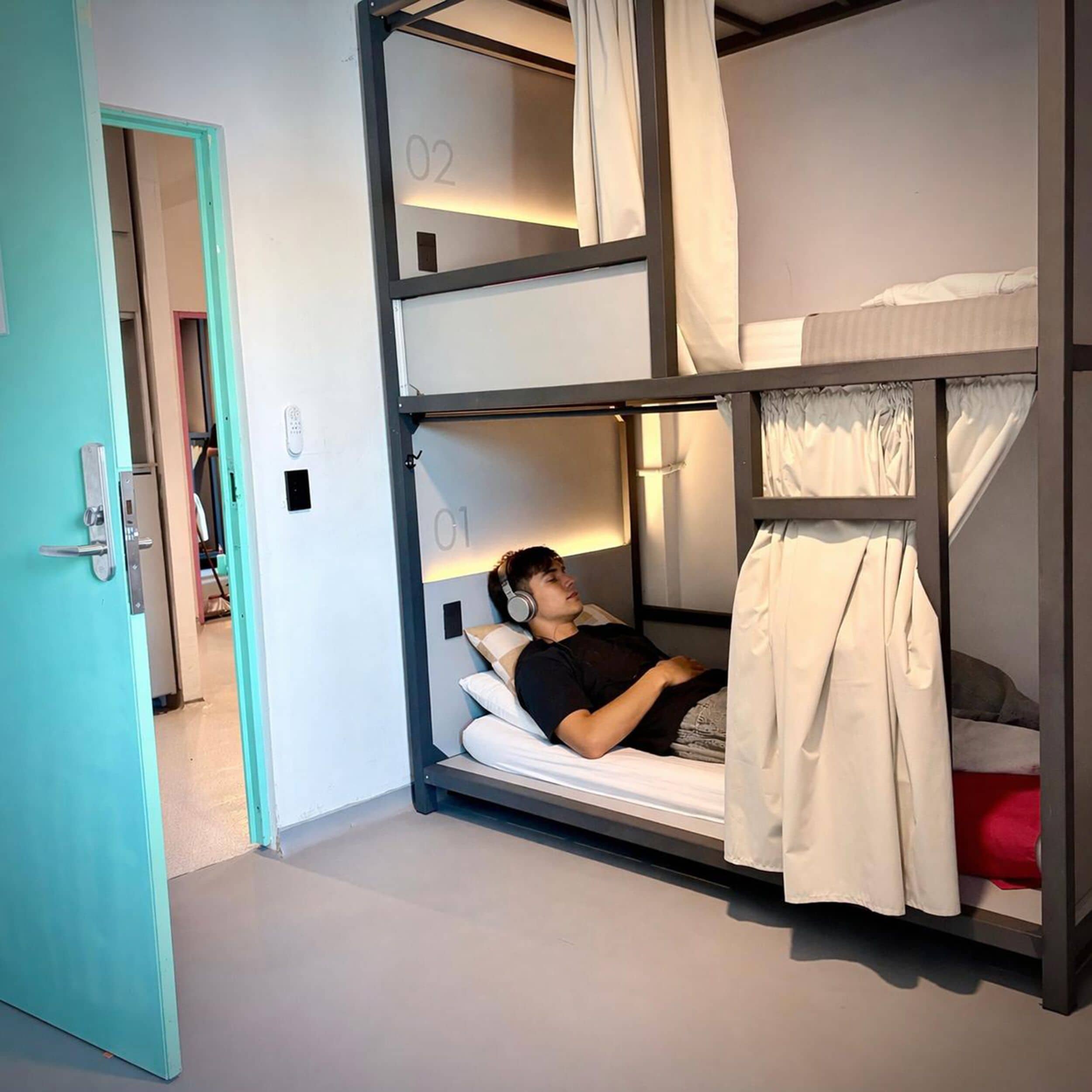 Habitación con literas, una persona acostada en la litera inferior, una puerta a la izquierda y el número '02' en la litera superior.