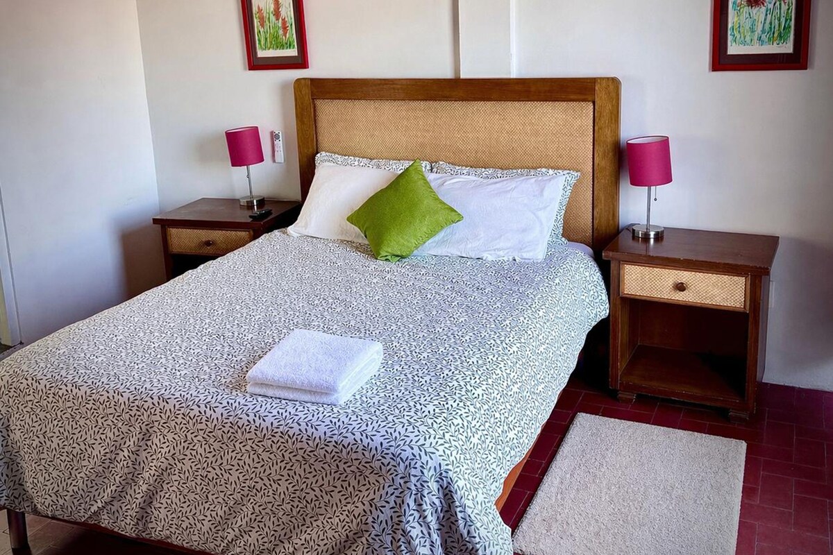 A neatly made bed with a patterned bedspread, two bedside lamps, and two framed pictures on the walls.