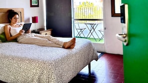 A room with a bed, a ceiling fan, a window with a view of the outside, and a door with a green frame. - Nube Mia Hostel (Guadalajara)